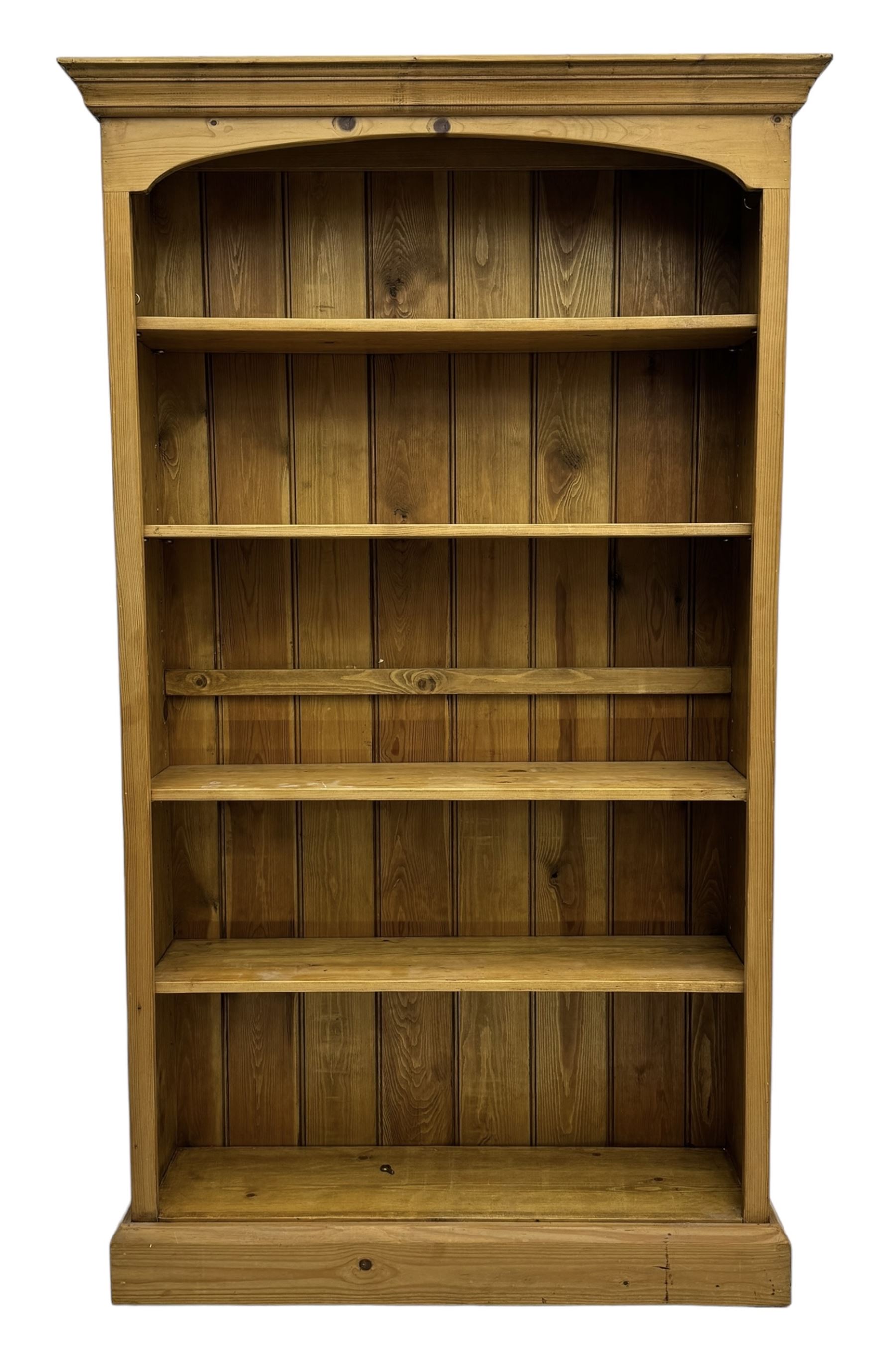 Pine open bookcase, projecting moulded cornice over arched frieze, fitted with four adjustable shelves, on plinth base