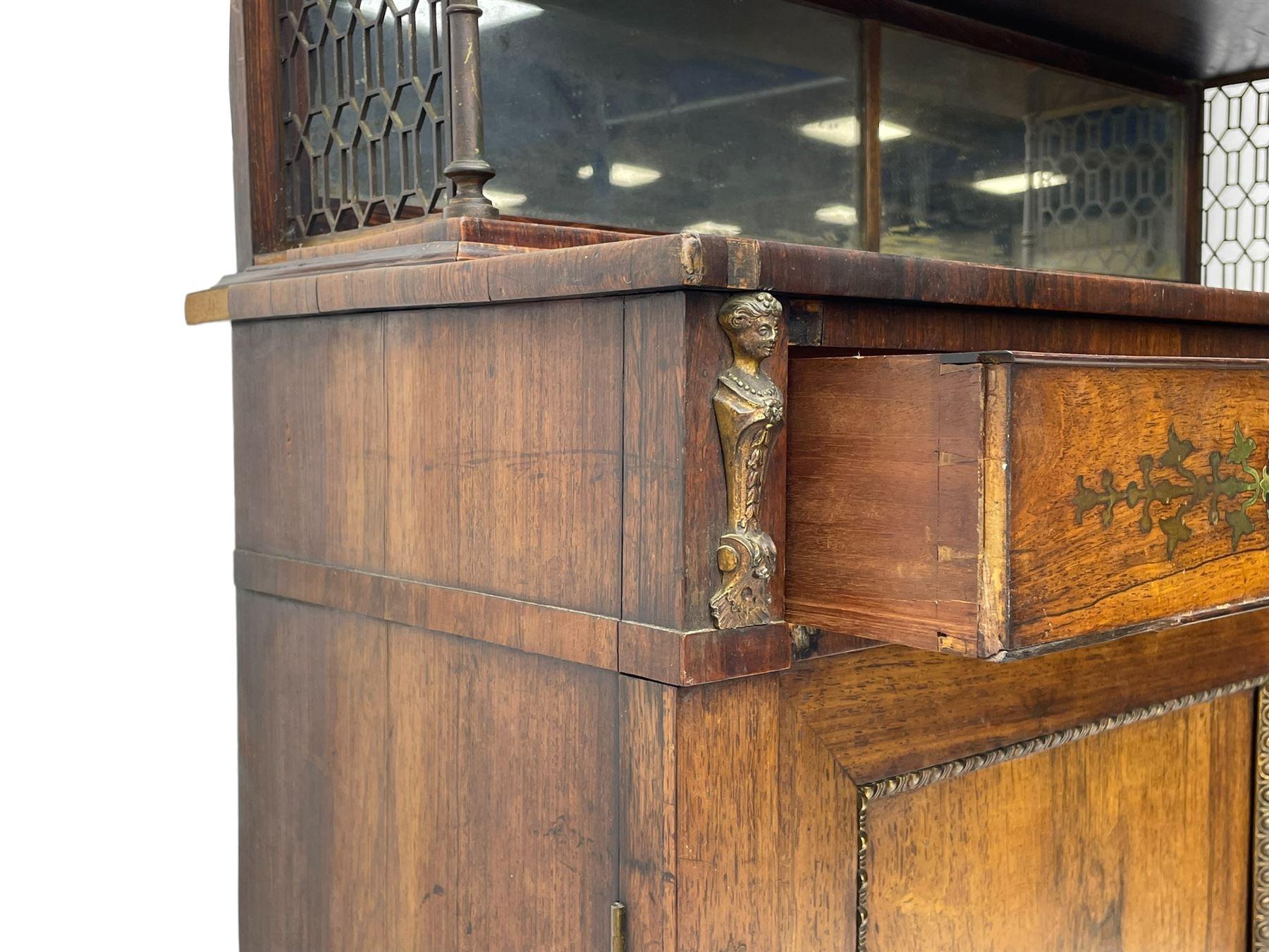 Attributed to John McLean & Son (London: 1770-1825) - Regency rosewood chiffonier, the raised two tier mirrored back on turned brass supports with brass trestle sides, rectangular top with brass stringing over two drawers and central cast brass satyr mask, cock-beaded drawer fronts inlaid with extending stylised foliate brass work, double cupboard below enclosed by panelled doors with cast egg and dart edging, matched brass inlays to the uprights, fitted with internal shelf, on turned compressed bun feet 