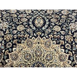 Persian Kashan indigo ground carpet, the central ivory rosette medallion surrounded by trailing and interlaced flower heads and branches, matching spandrels with floral design, the border with scrolling pattern decorated with stylised plant motifs within guards