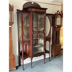 Art Nouveau period inlaid mahogany display cabinet, raised shaped and moulded pediment over projecting moulded cornices, the upper frieze inlaid with trailing branches and tulips, single astragal and bevel glazed door enclosed velvet lined interior fitted with shelves, flanked by curved glass panes decorated with pierced metal foliate spandrels, lower flanking shelves with mirror backs enclosed within shaped and pierced rails inlaid with flower heads, on tapering octagonal supports terminating to compressed pad feet, the lock stamped 'Salmon Bros, London' 