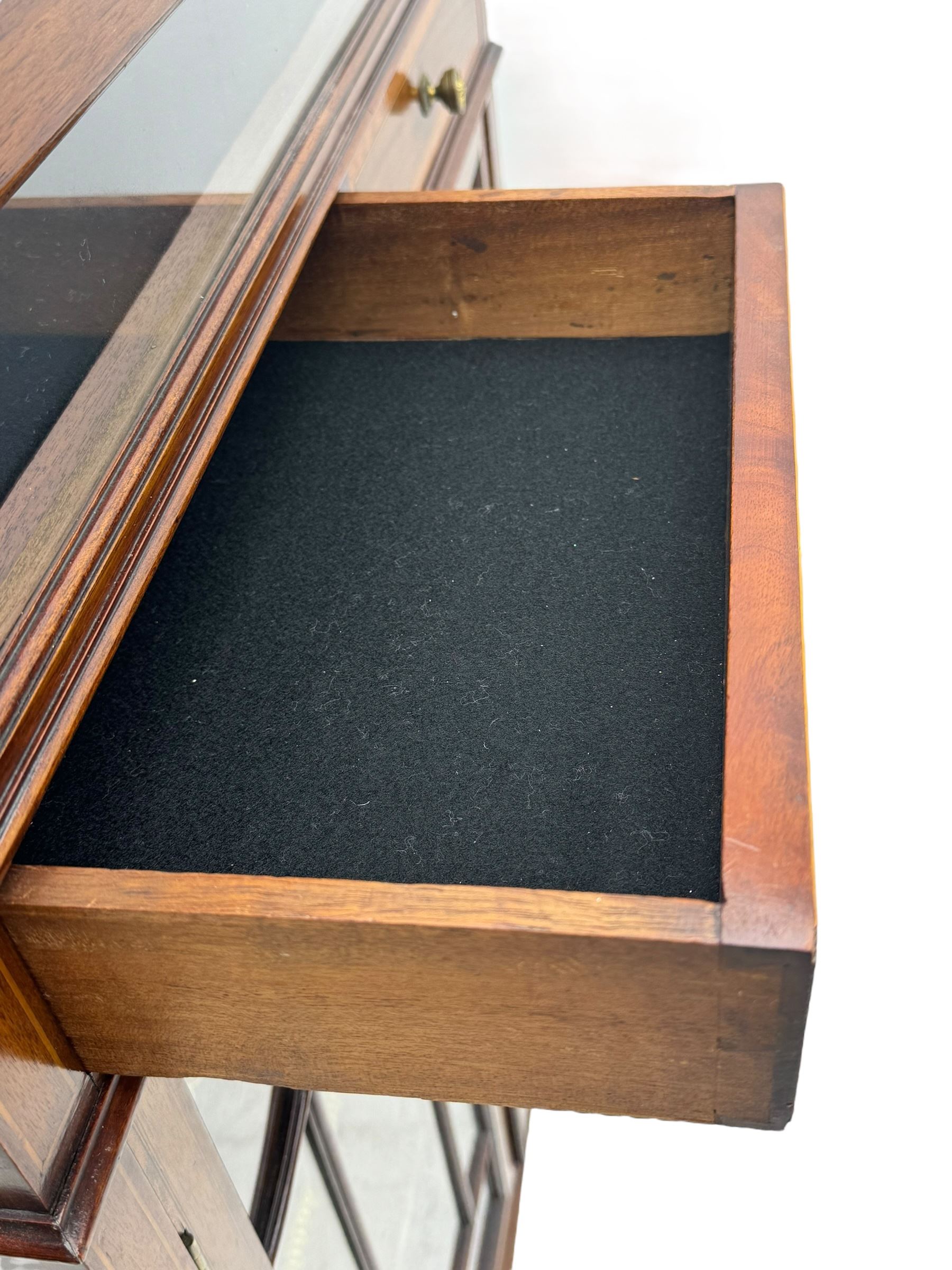 Edwardian mahogany bijouterie display cabinet, featuring satinwood inlay and crossbanding, hinged glazed top fitted with two banded drawers, over two astragal glazed doors enclosing black wool baize lined shelves with gold trim, supported by spade feet