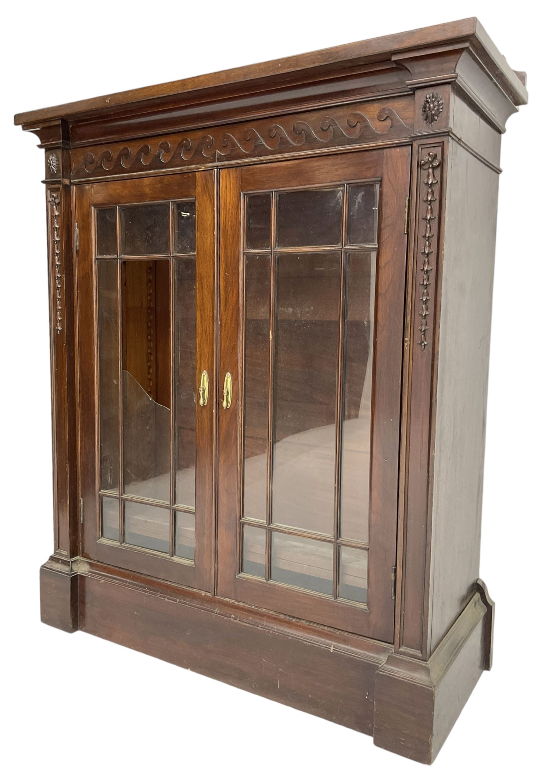 19th century mahogany display cabinet, rectangular top over frieze decorated with Vitruvian scroll mount, enclosed by two astragal glazed doors, the upright rails decorated with trailing bellflowers, on moulded plinth