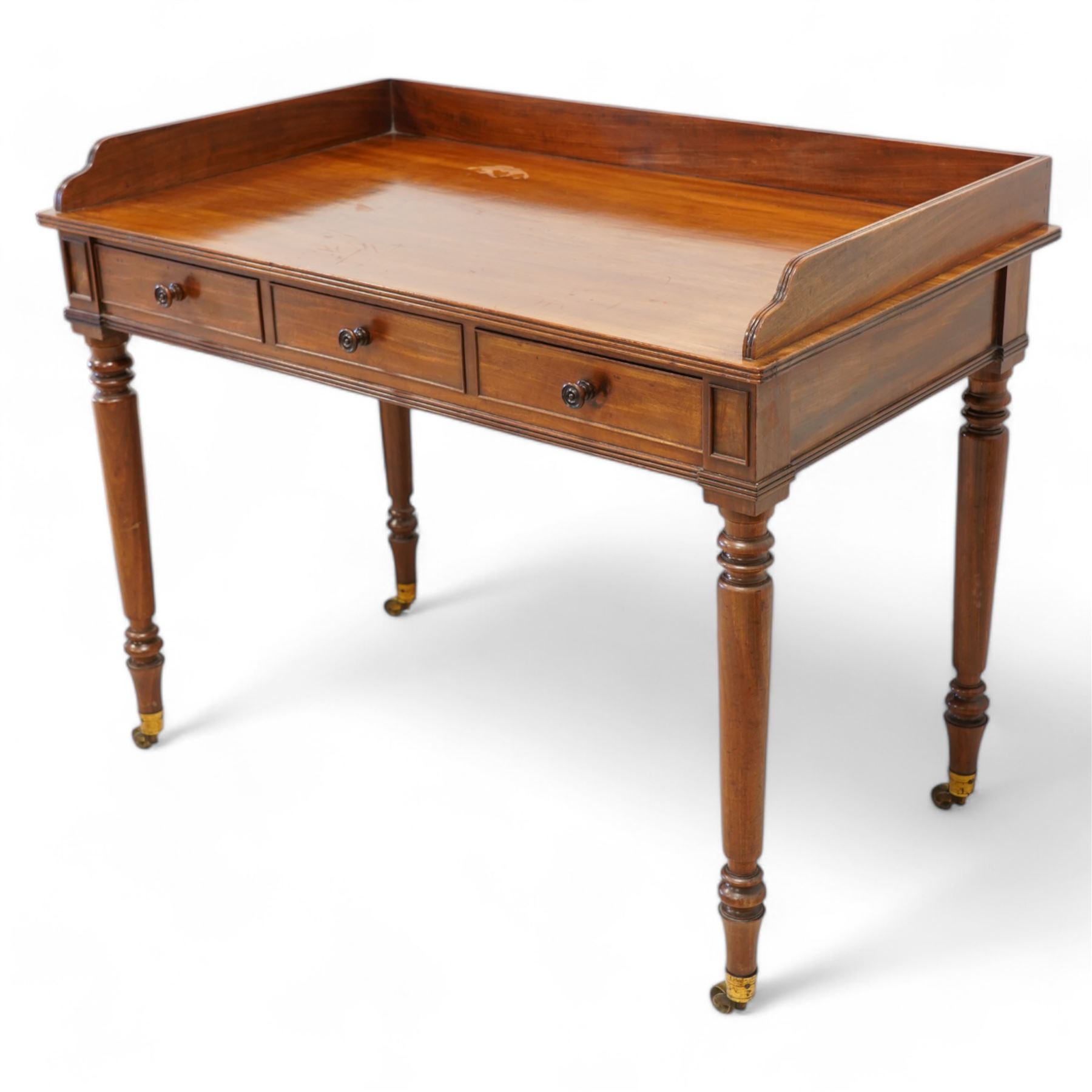 Gillows, Lancaster - early 19th century mahogany writing table, reeded three-quarter gallery over rectangular top with reed moulded edge, fitted with three cocked-beaded drawers with turned handles, the central drawer stamped 'Gillows Lancaster'. on turned supports with brass cups and castors 