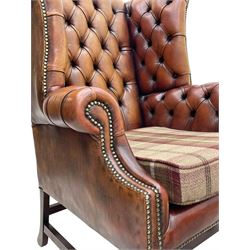 Georgian design hardwood-framed wingback armchair, shaped cresting rail and deep wingback over rolled arms, upholstered in brown buttoned leather with studwork bands, the seat cushion upholstered in checkered fabric, on square supports united by stretchers (W86cm, H118cm, D86cm); together with matching rectangular footstool (63cm x 43cm, H37cm) 