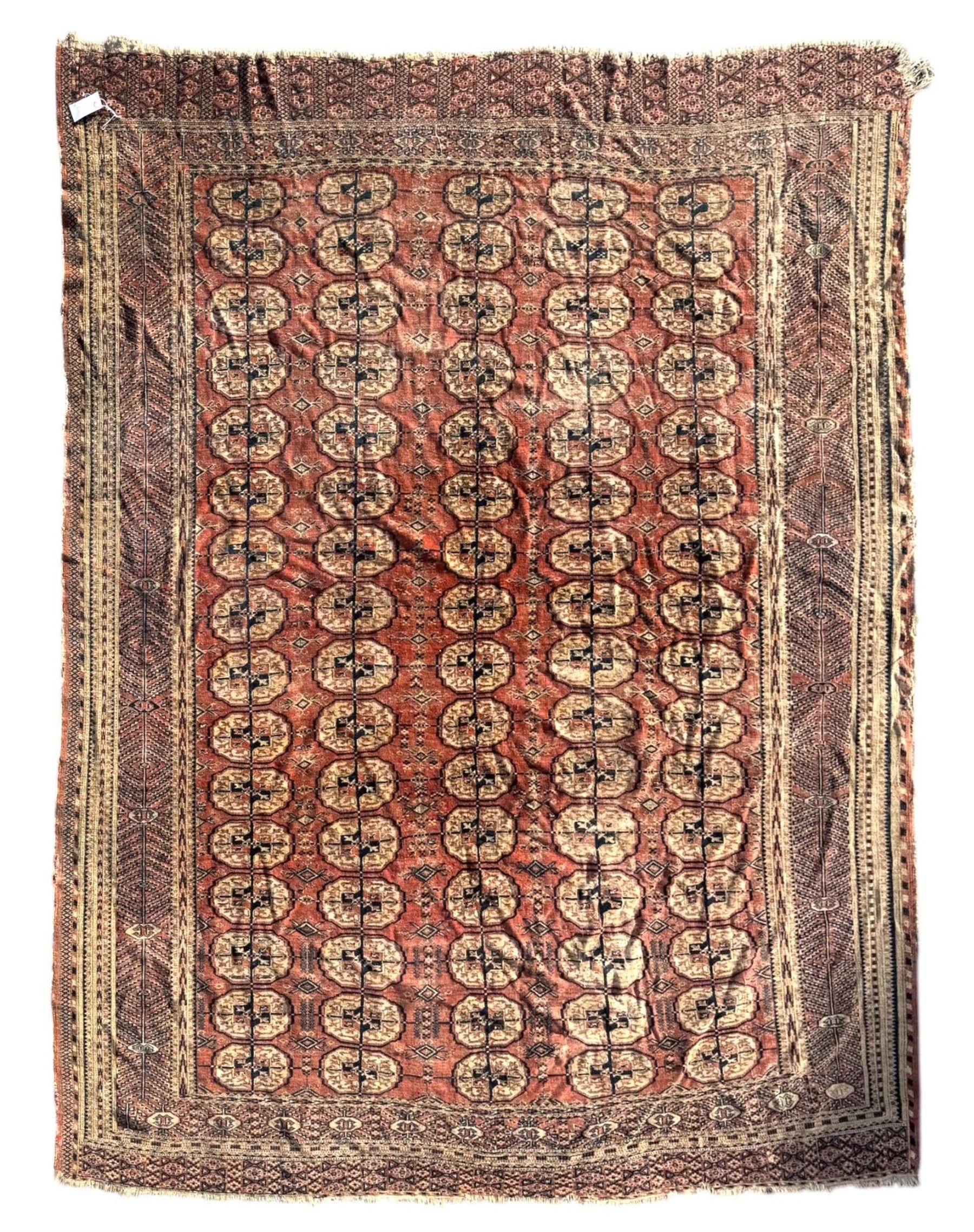 Bokhara red ground carpet, the central field featuring a repeating pattern of traditional octagonal guls arranged in vertical rows, bordered by multiple guard bands with geometric designs, finished with fringed ends