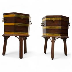 Pair of George III mahogany and brass bound cellarettes or wine coolers on stands, hexagonal form, moulded hinged lid enclosing metal lining, the body strapped in brass bands and fitted with carrying handles, the stand with moulded upper rails on splayed and moulded square supports with castors, with arched corner brackets 