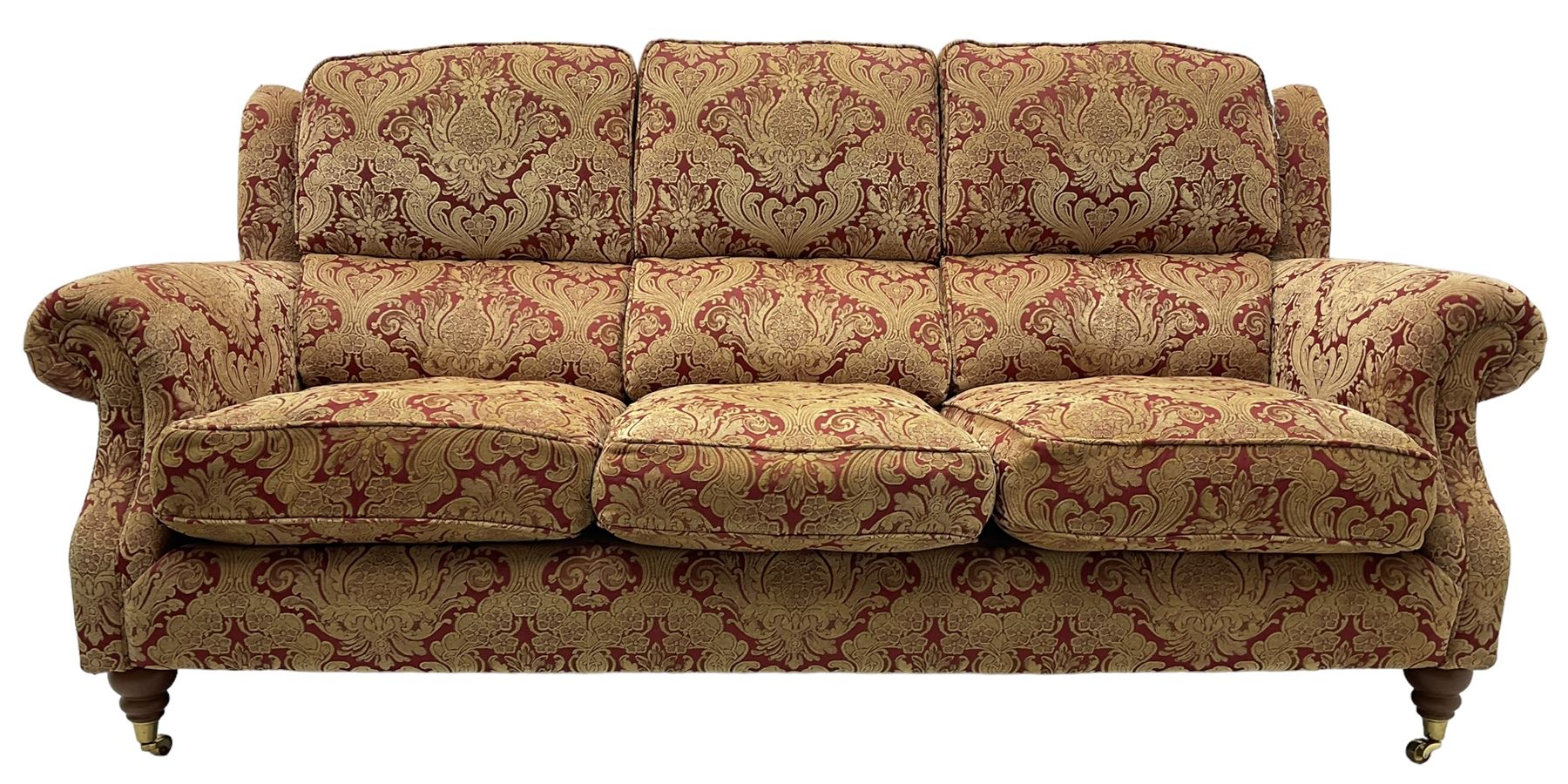 Parker Knoll - three-seat 'Oakham' hardwood-framed sofa, upholstered in red and gold floral pattern fabric, on turned feet with brass cups and castors 