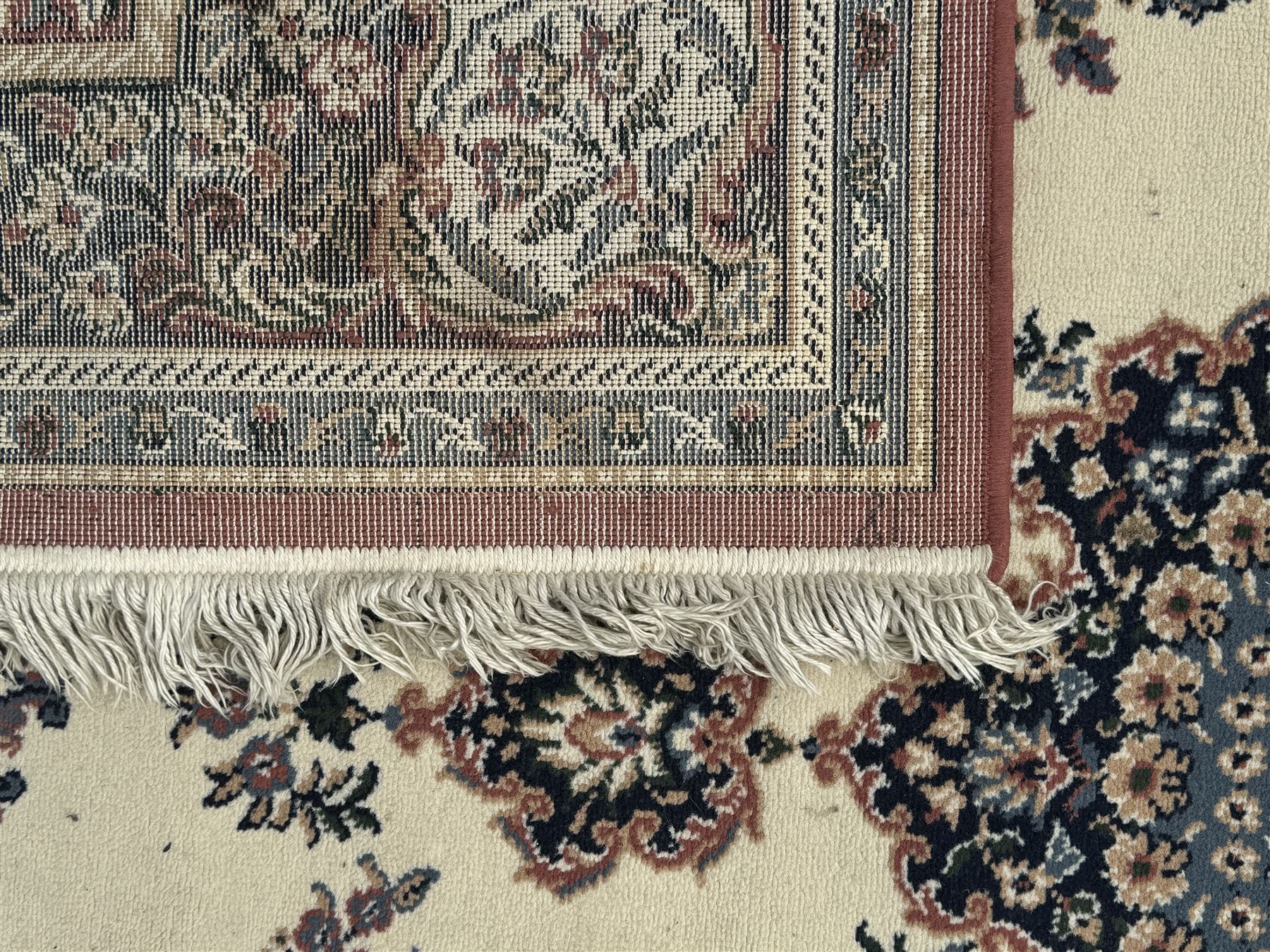 Persian design ivory ground rug, the field decorated with an oval medallion filled with floral motifs and scrolling vines, flanked by floral sprays and corner spandrels with palmette designs, the main border featuring a series of stylised floral patterns against a dark blue ground, enclosed by multiple guard stripes with geometric and floral motifs