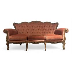 Late 20th century French walnut framed three-seat sofa, high shaped back with floral carved cresting rail, deep-buttoned coral velvet upholstery with loose seat cushions, scrolling arm terminals over moulded walnut frame, raised on cabriole supports