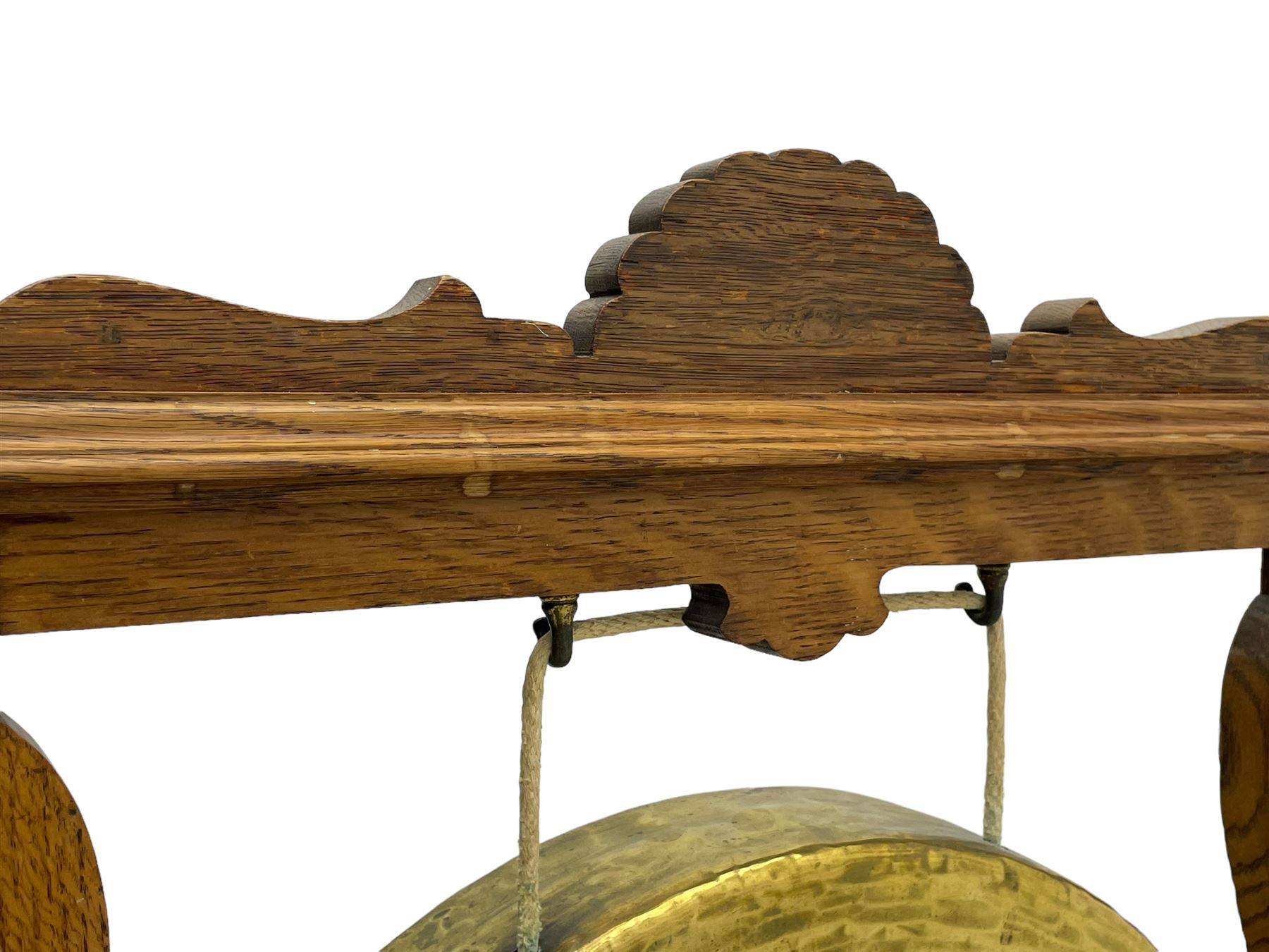 Early 20th century oak gong stand with gong and hammer, shaped cresting rail over moulded upper edge on shaped supports, hanging brass drum gong over fretwork middle rail, on raised platforms terminating to splayed feet