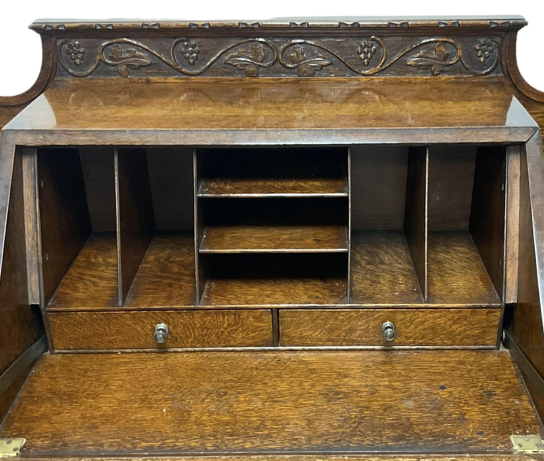 Early 20th century heavily carved oak bookcase bureau, raised back with grape-vine carved frieze, over fall-front enclosing fitted interior, above two short drawers and curved frieze drawer, flanked by astragal glazed and panelled cupboards, on turned feet