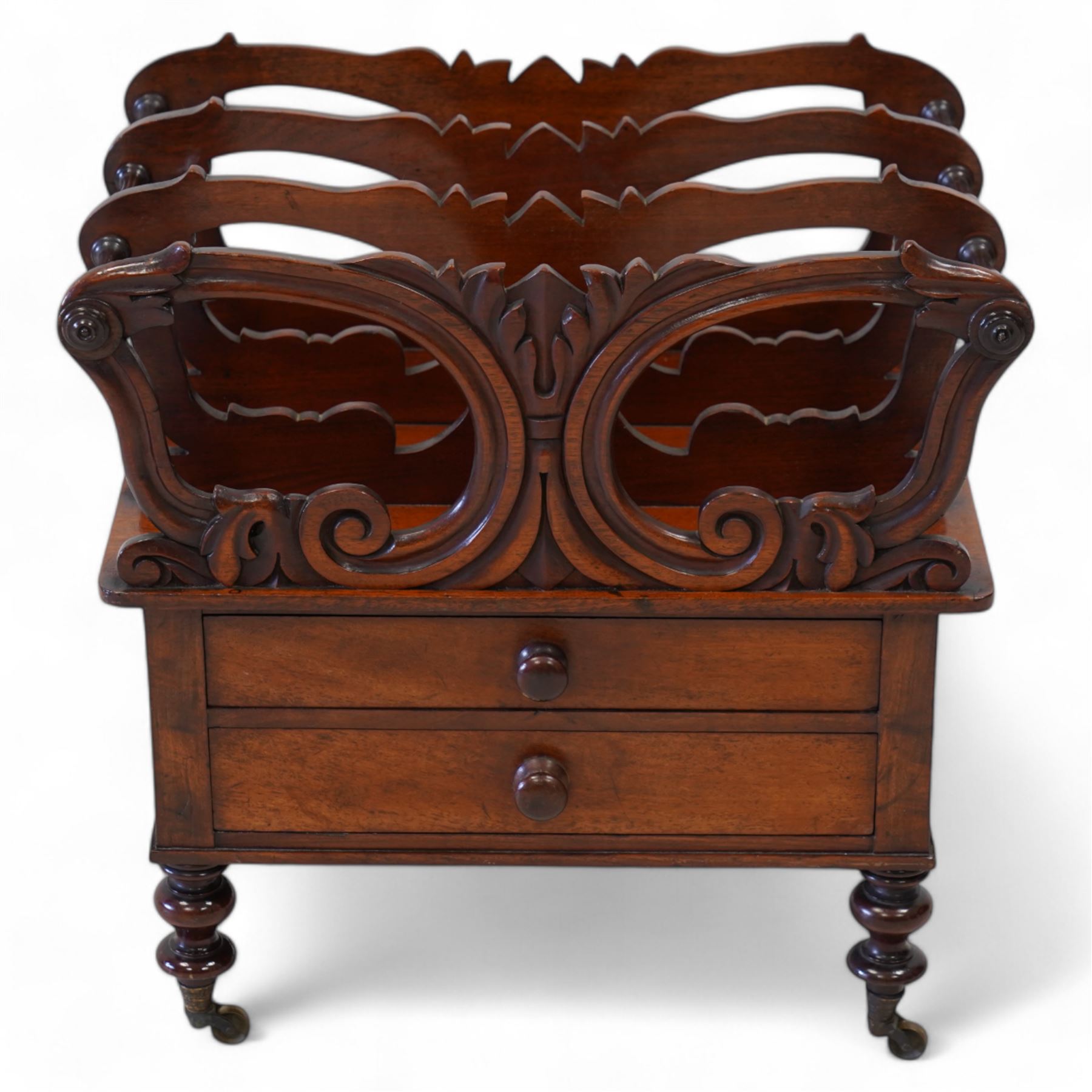 Victorian mahogany Canterbury, three divisions, carved with scrolls and curled leaf motifs, fitted with two drawers, on turned feet with brass cups and castors 