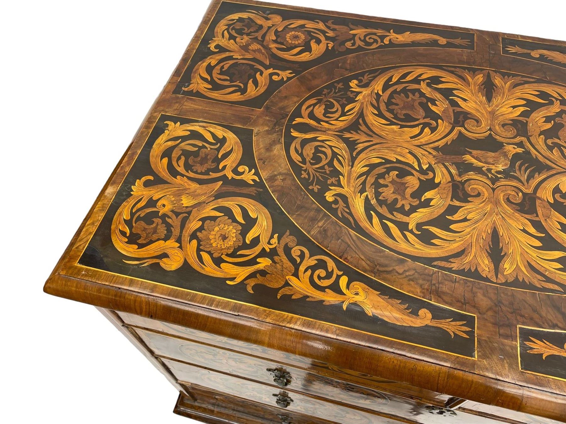 18th century inlaid walnut chest on stand, ovolo-moulded rectangular top inlaid with ebony panels each decorated with scrolling foliage, flower heads and birds, fitted with two short over three long drawers, the drawer fronts decorated with ebony panels enclosing curled leaf inlays, the base fitted with single drawer on turned supports united by waved stretchers, on turned bun feet 