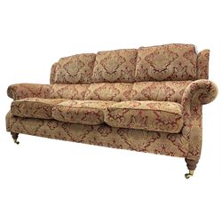 Parker Knoll - three-seat 'Oakham' hardwood-framed sofa, upholstered in red and gold floral pattern fabric, on turned feet with brass cups and castors 