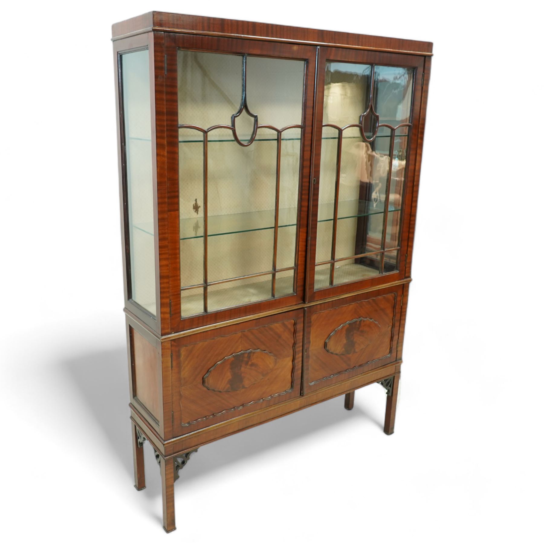 Early 20th century mahogany display cabinet, enclosed by astragal glazed doors over two scalloped panelled cupboard doors, on square supports with pierced scrolling brackets