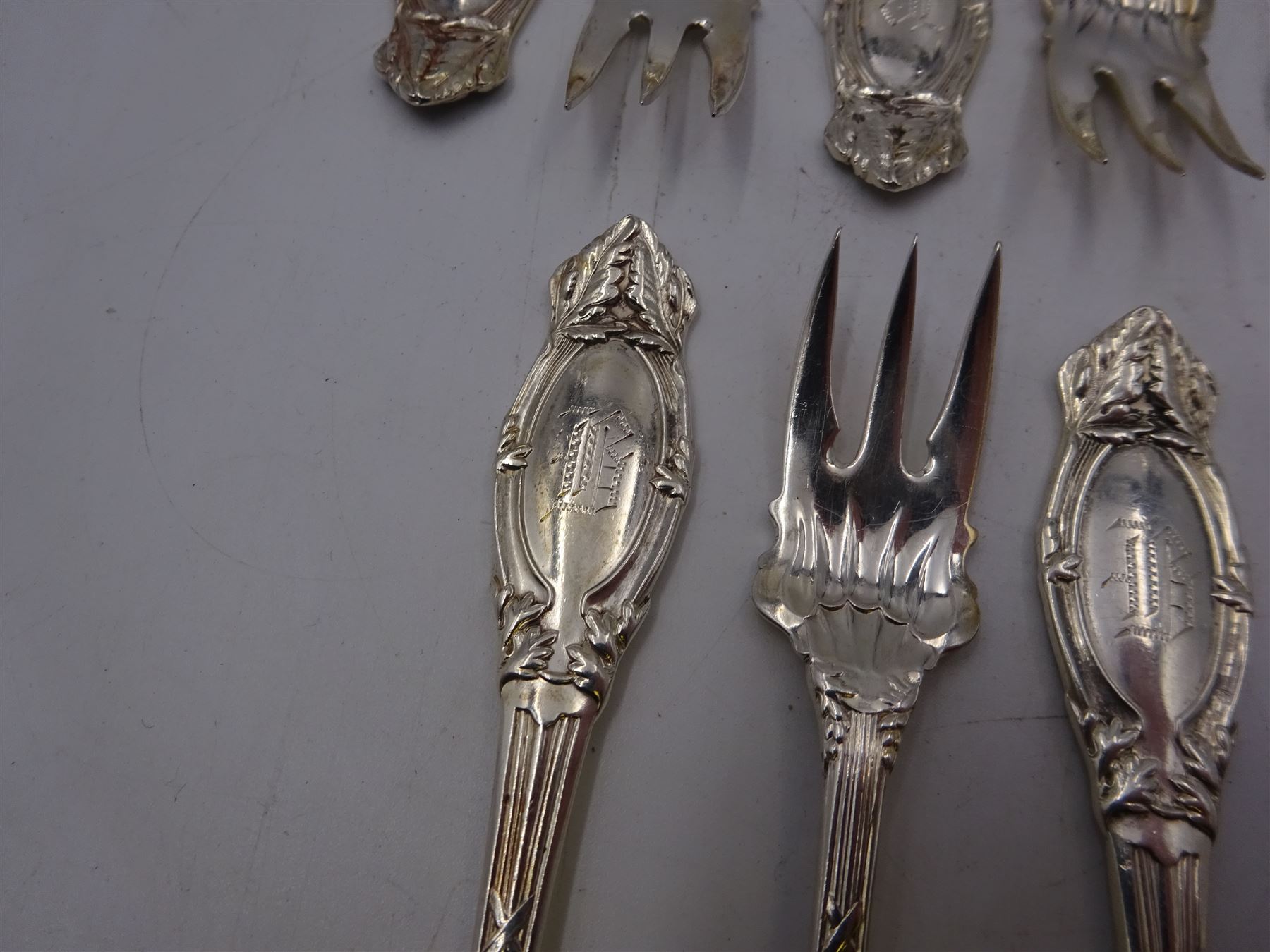 Set of twelve American silver oyster/pickle forks, three pronged forks, the stem decorated with ribbon banding and foliate border surrounding an engraved initial, stamped Sterling 