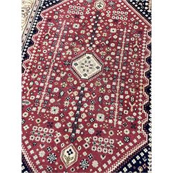 Persian design crimson ground rug, the field decorated with tree of life and floral motifs, enclosed by indigo spandrels with stylised flower head decoration, repeating scrolling border 