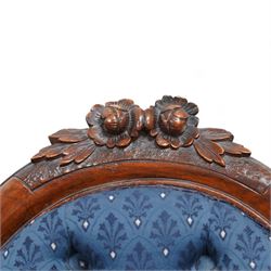 Victorian carved walnut framed nursing chair, the cresting carved with flower heads and extending foliage, upholstered in buttoned blue fabric with repeating pattern, on floral carved cabriole feet