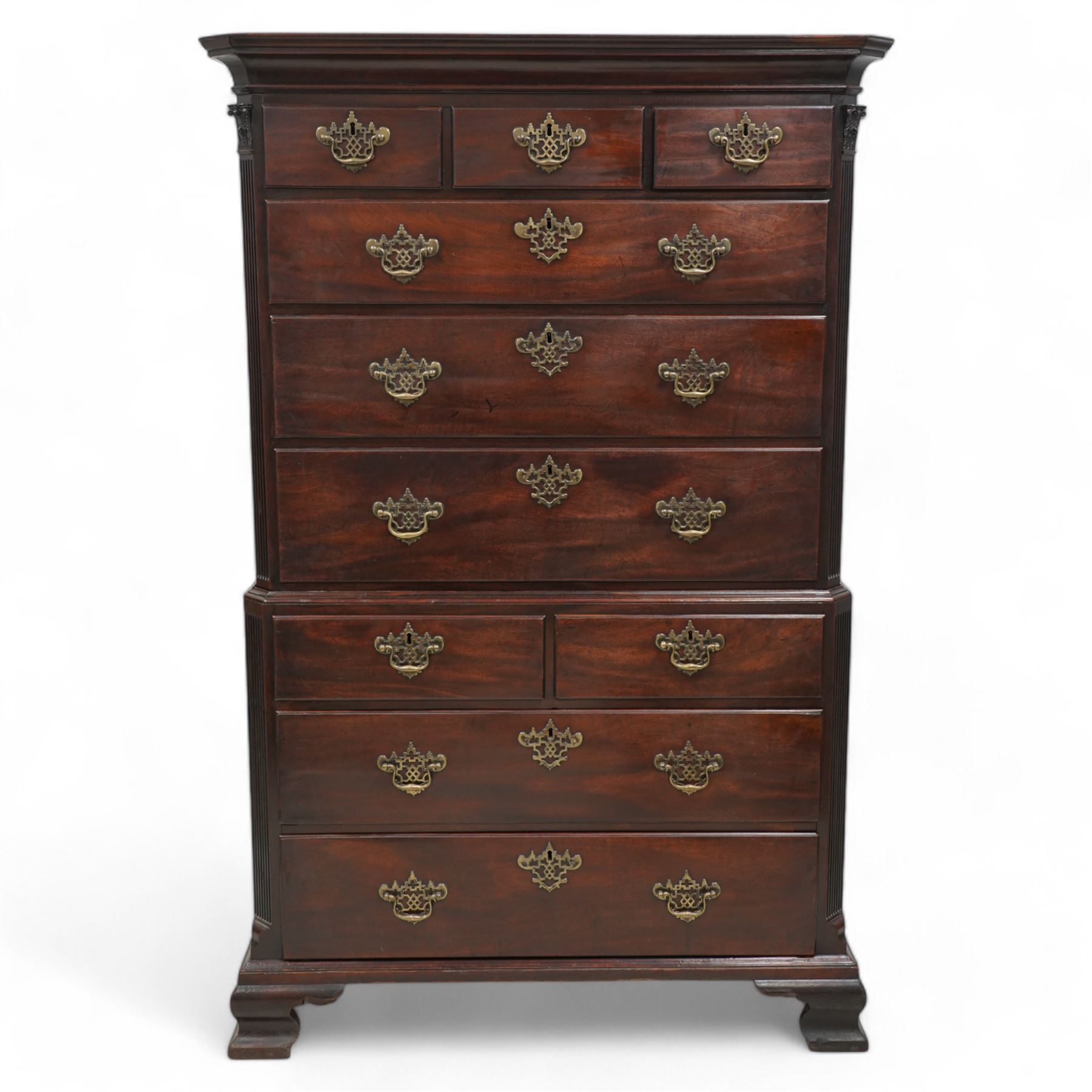 George III mahogany chest-on-chest, canted rectangular form, stepped cavetto moulded cornice, the upper section fitted with three short over three long drawers, the lower section fitted with two short over two long drawers, moulded drawer fronts with shaped and pierced handles plates and swan neck handles, enclosed by fluted corners with acanthus leaf capitals, on ogee bracket feet