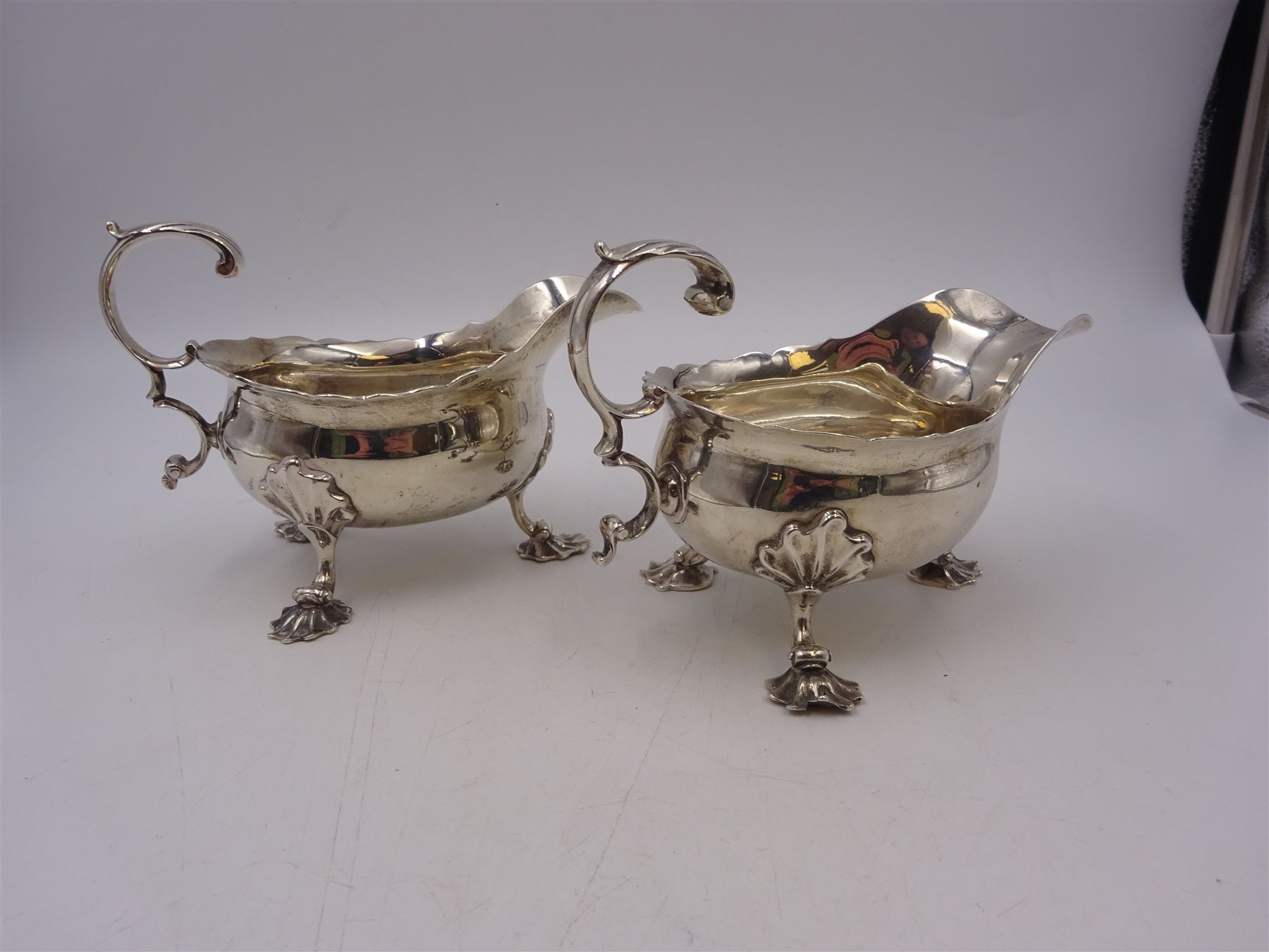 Near pair of George II silver sauce boats, each of oval form with shaped rim and capped flying scroll handle, upon three scroll mounted feet, hallmarked David Hennell, London 1758, H12cm