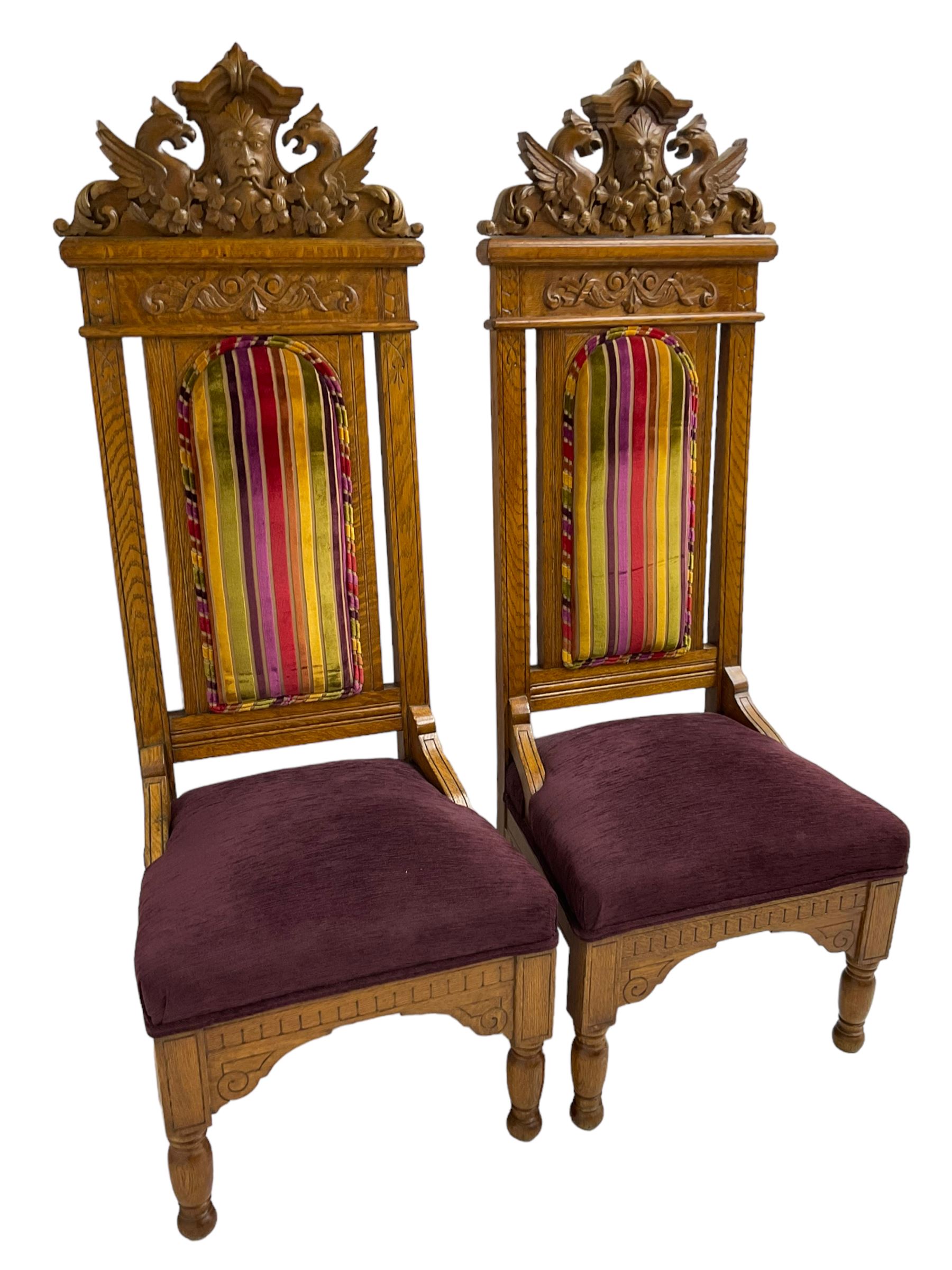 Set of six 20th century Carolean design oak high back chairs, the pediment carved with dragons and central Green Man mask with trailing foliage, the backs upholstered in striped fabric, on turned front supports