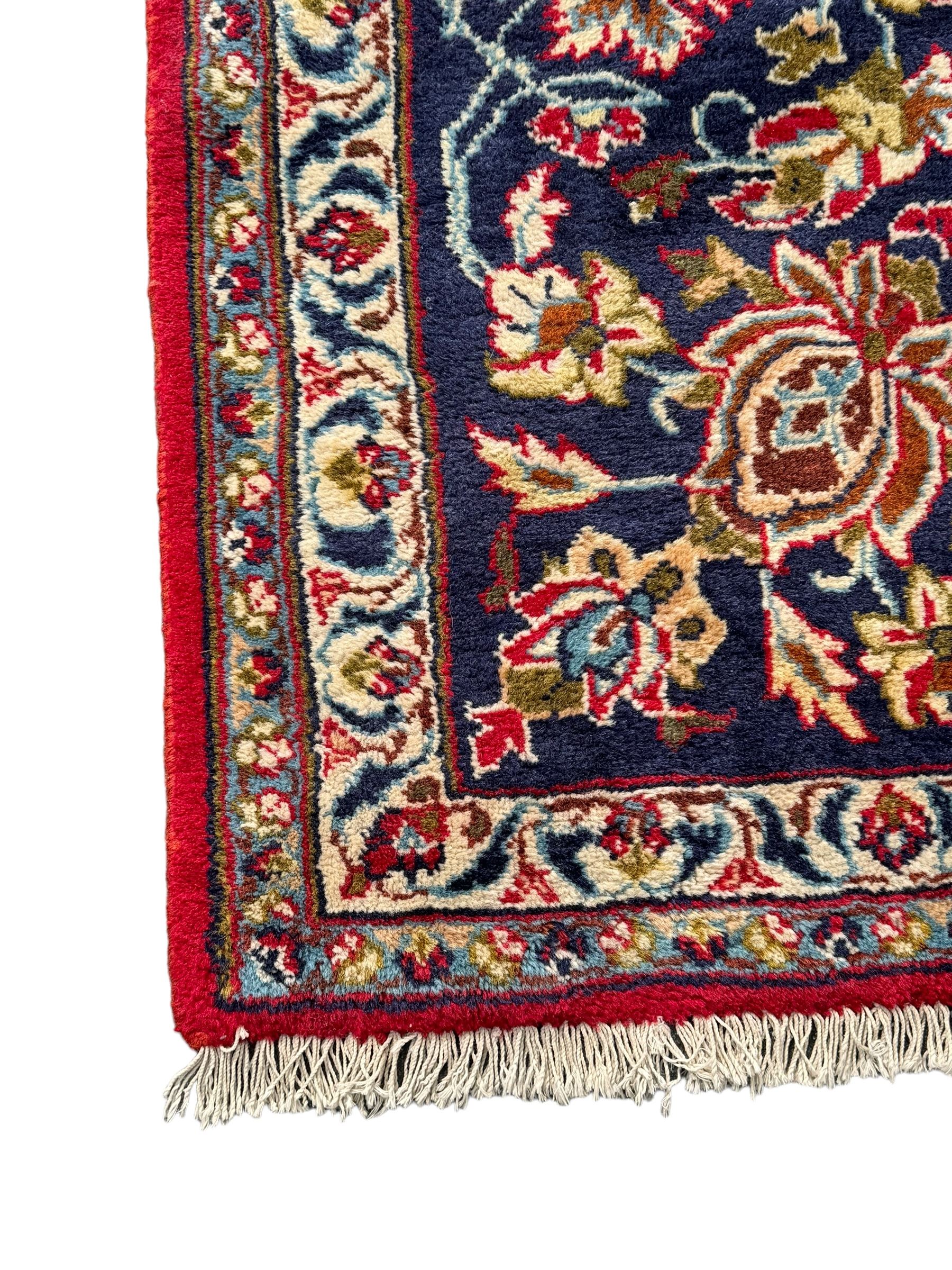 Persian Kashan red ground rug, the field decorated with a central floral medallion surrounded buy scrolling vine motifs and palmettes, the main border featuring a series of stylised floral motifs against a dark blue ground, enclosed by multiple guard stripes with alternating floral and geometric designs