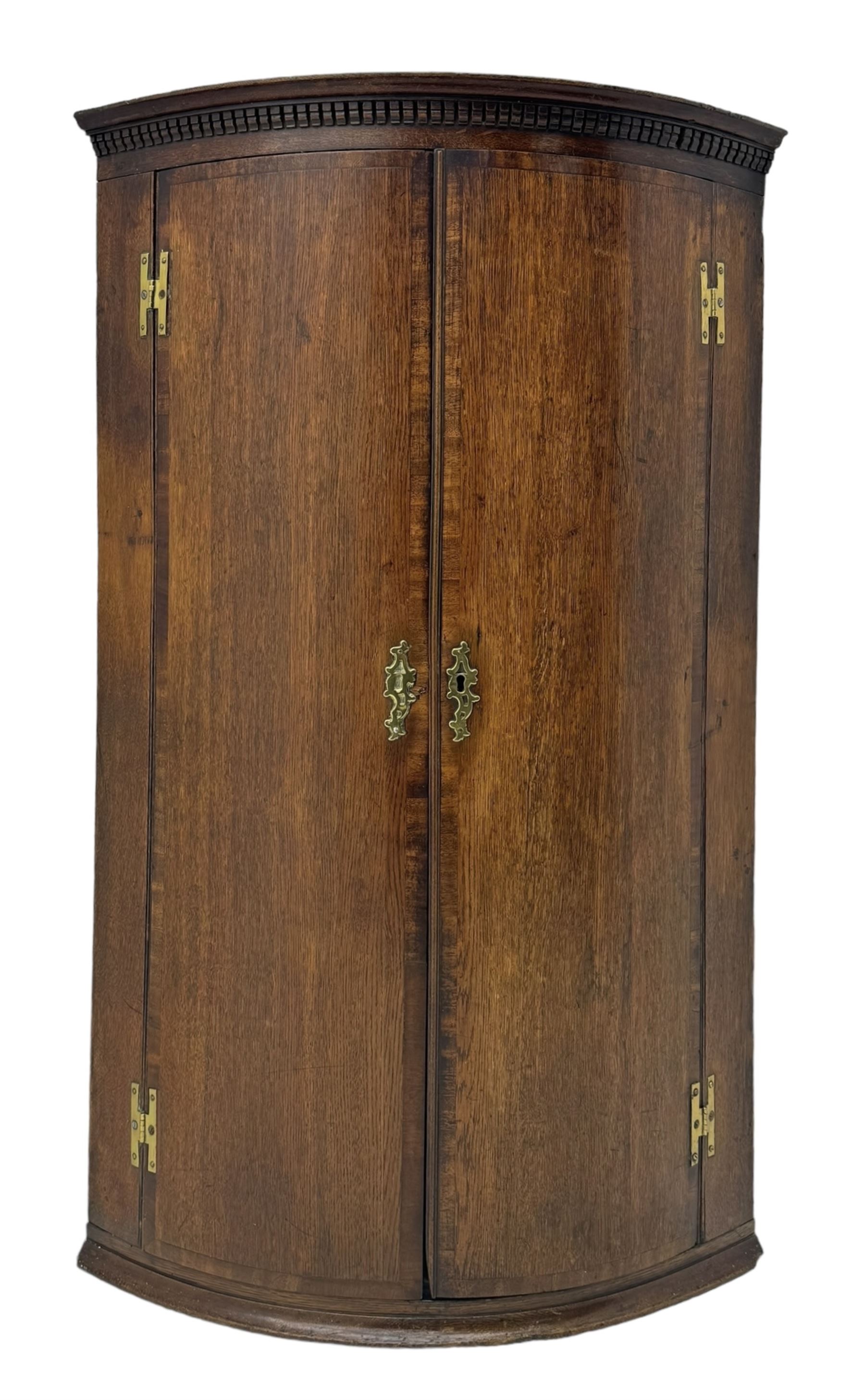 Georgian oak corner cabinet, projecting cornice with shaped dentil frieze, over two panelled doors enclosing three shelves, on a plain plinth base