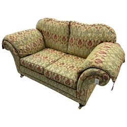 Traditional design two seat sofa, high back with scrolled arms, upholstered in beige fabric with red and green damask motifs, on castor supports (L178cm, D100cm, H89cm); matching armchair (L109cm, D89cm, H89cm)