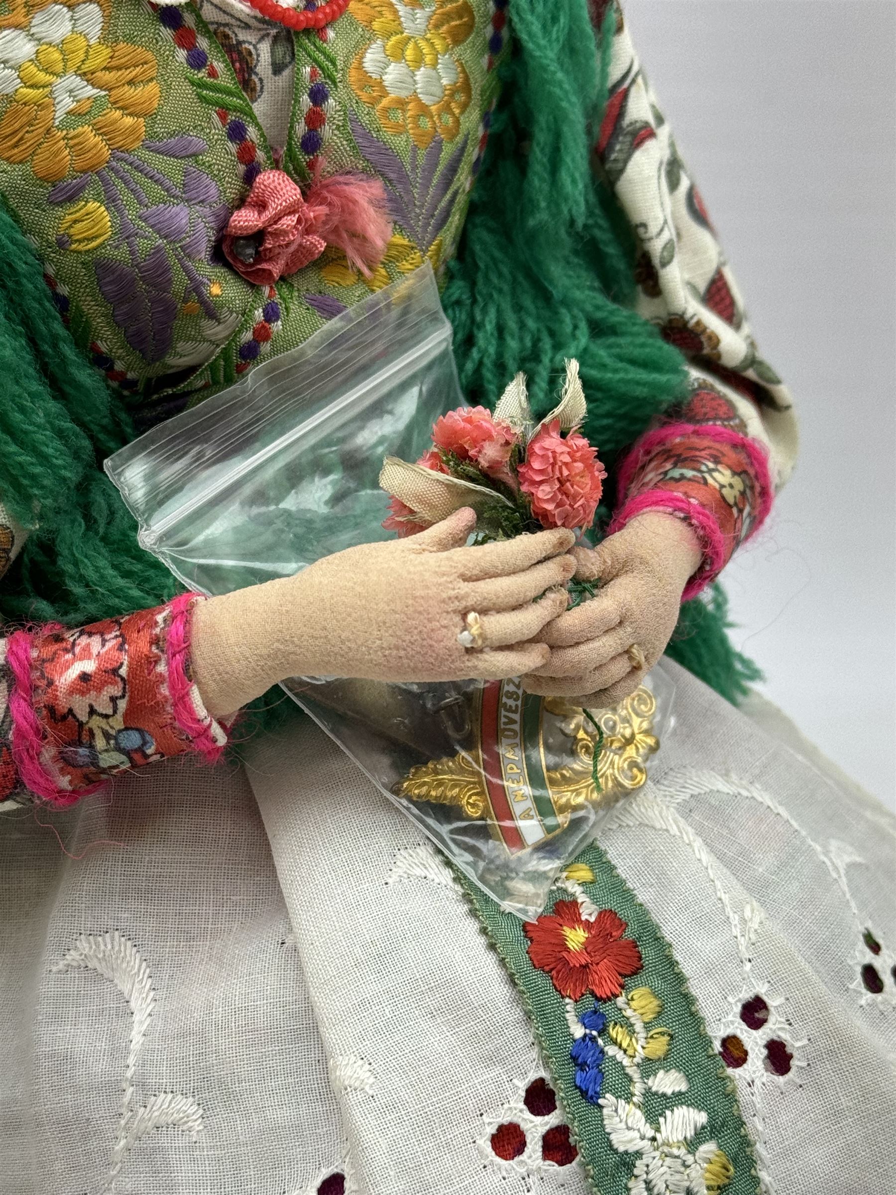 Anna Meszaros (Hungarian 1905-1998): Young Woman Holding Flowers, handmade needlework figurine, together with two badges awarded to the artist in needlework competitions, figure H29cm
Auctioneer's Note: Anna Meszaros came to England from her native Hungary in 1959 to marry an English businessman she met while demonstrating her art at the 1958 Brussels Exhibition. Shortly before she left for England she was awarded the title of Folk Artist Master by the Hungarian Government. Anna was a gifted painter of mainly portraits and sculptress before starting to make her figurines which are completely hand made and unique, each with a character and expression of its own. The hands, feet and face are sculptured by layering the material and pulling the features into place with needle and thread. She died in Hull in 1998