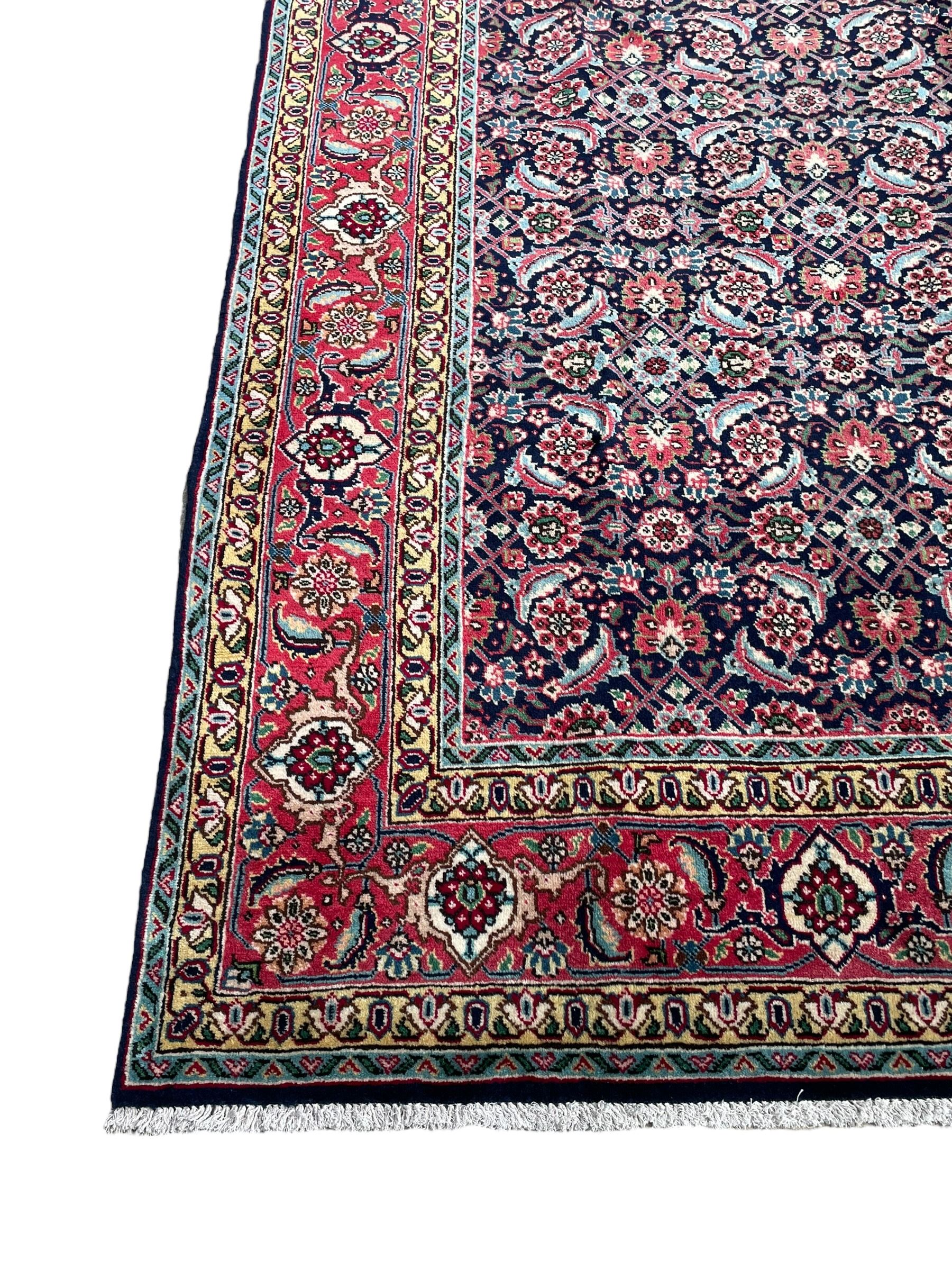 Persian Farahan indigo ground rug, the field decorated with large repeating floral herati motifs, crimson ground border decorated with palmettes and trailing leafy branch, within guard stripes 