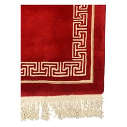 Chinese washed woolen red ground rug, central circular dragon motif in ivory, framed by a decorative Greek key border in matching ivory tones, finished with fringed ends