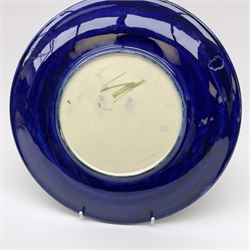 A Moorcroft plate decorated in the magnolia pattern upon a dark blue glazed ground, with impressed and painted marks beneath, D26cm. 
