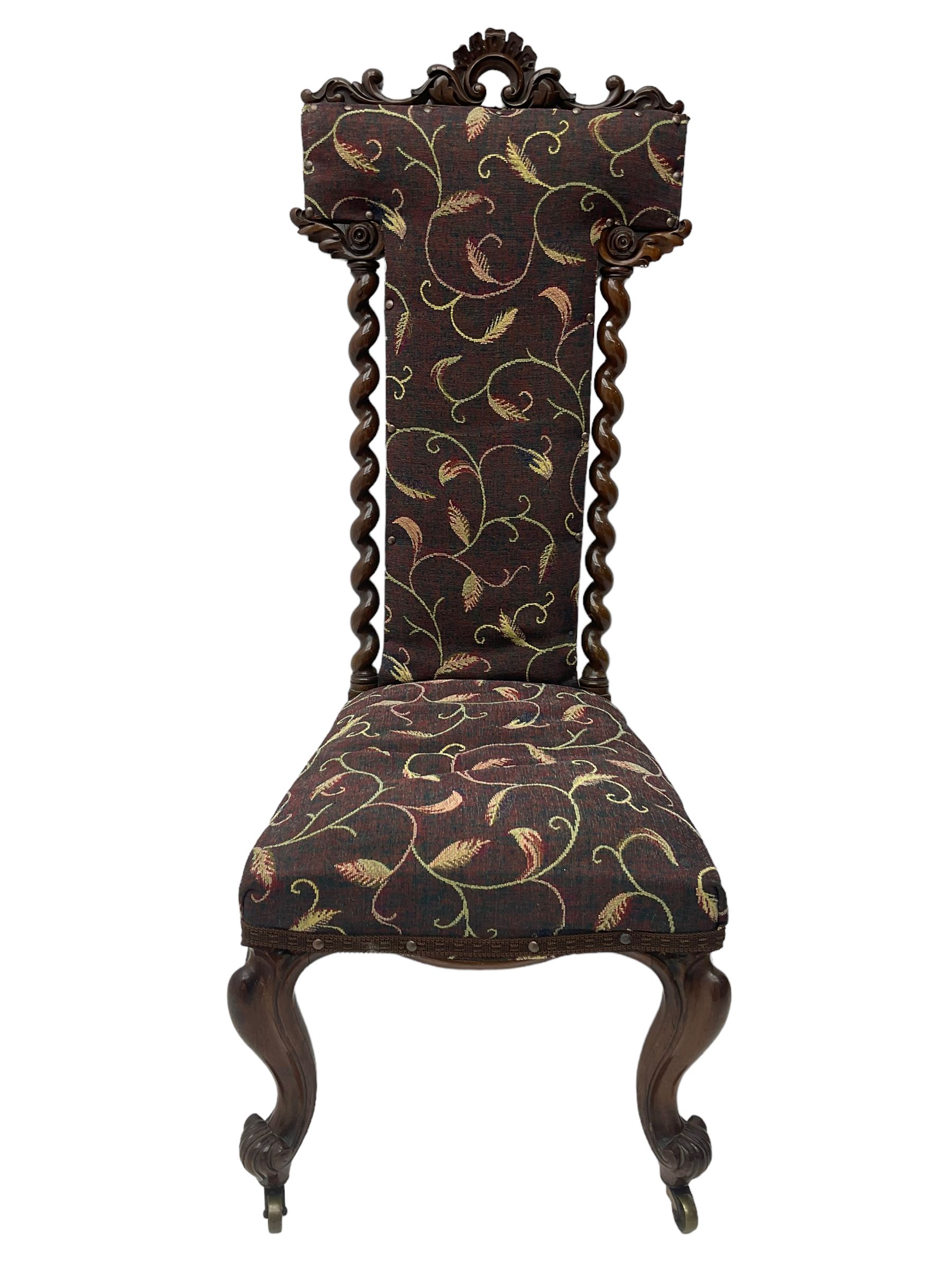 Victorian walnut prie-dieu chair, cresting rail carved with cartouche and extending scrolling foliage, back flanked by spiral turned column uprights, upholstered in foliate patterned fabric, raised on cabriole supports with scroll feet and castors