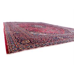 Large Kashan crimson ground carpet, central indigo medallion with stylised floral motifs, flanked by matching spandrels, bordered by multiple bands featuring repeating foliate and floral designs throughout