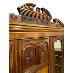 Victorian mahogany triple wardrobe, the pediment relief carved with urn and linen swags, the central panelled door carved with two fan motifs enclosing slides and drawers, two mirror glazed doors with bevelled plates enclosing hangings space and drawers, plinth base