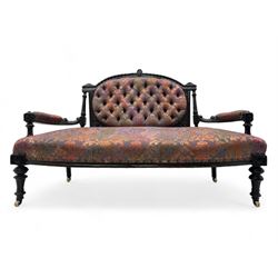 Late Victorian ebonised oak sofa, upholstered in muted purple fabric with iridescent floral pattern and nailhead trim, button-tufted backrest with carved crest rail and turned finials, scrolled padded arms supported by turned uprights, on turned supports with ceramic castors