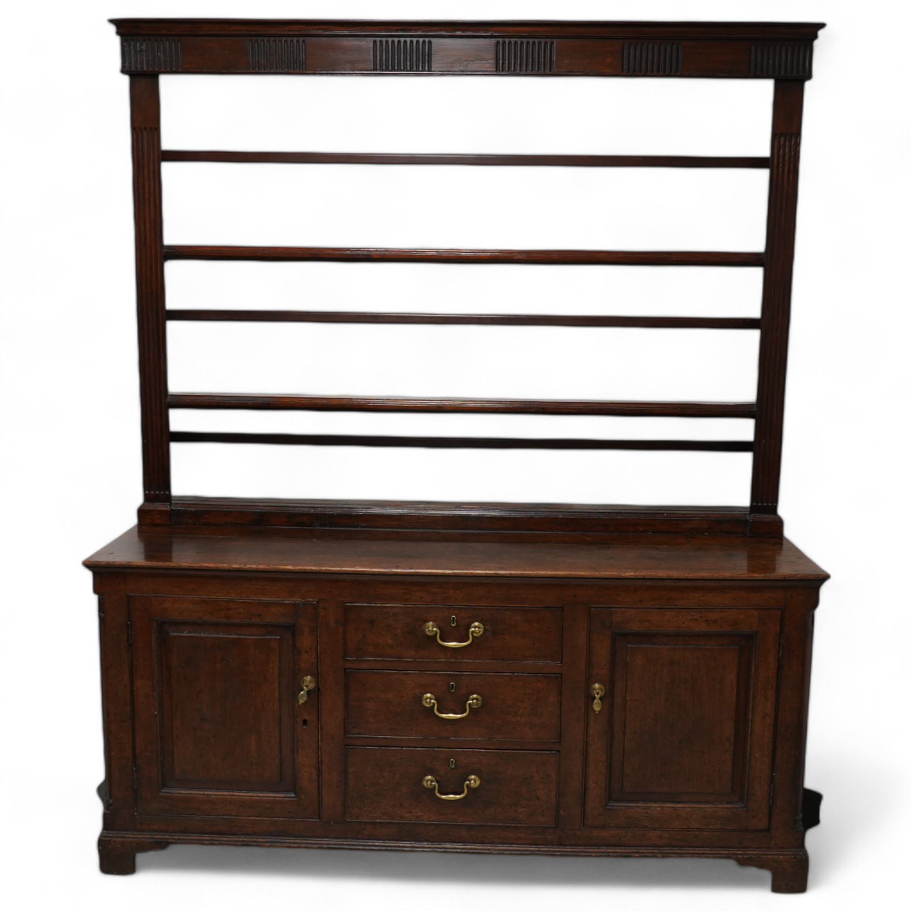 George III oak dresser, rectangular top, fitted with three central graduating cock-beaded drawers, flanked by panelled cupboards with quarter-canted pilaster uprights, lower moulded edge on bracket feet; with associated stained pine plate rack, carved with fluted detail (W170cm H124cm)