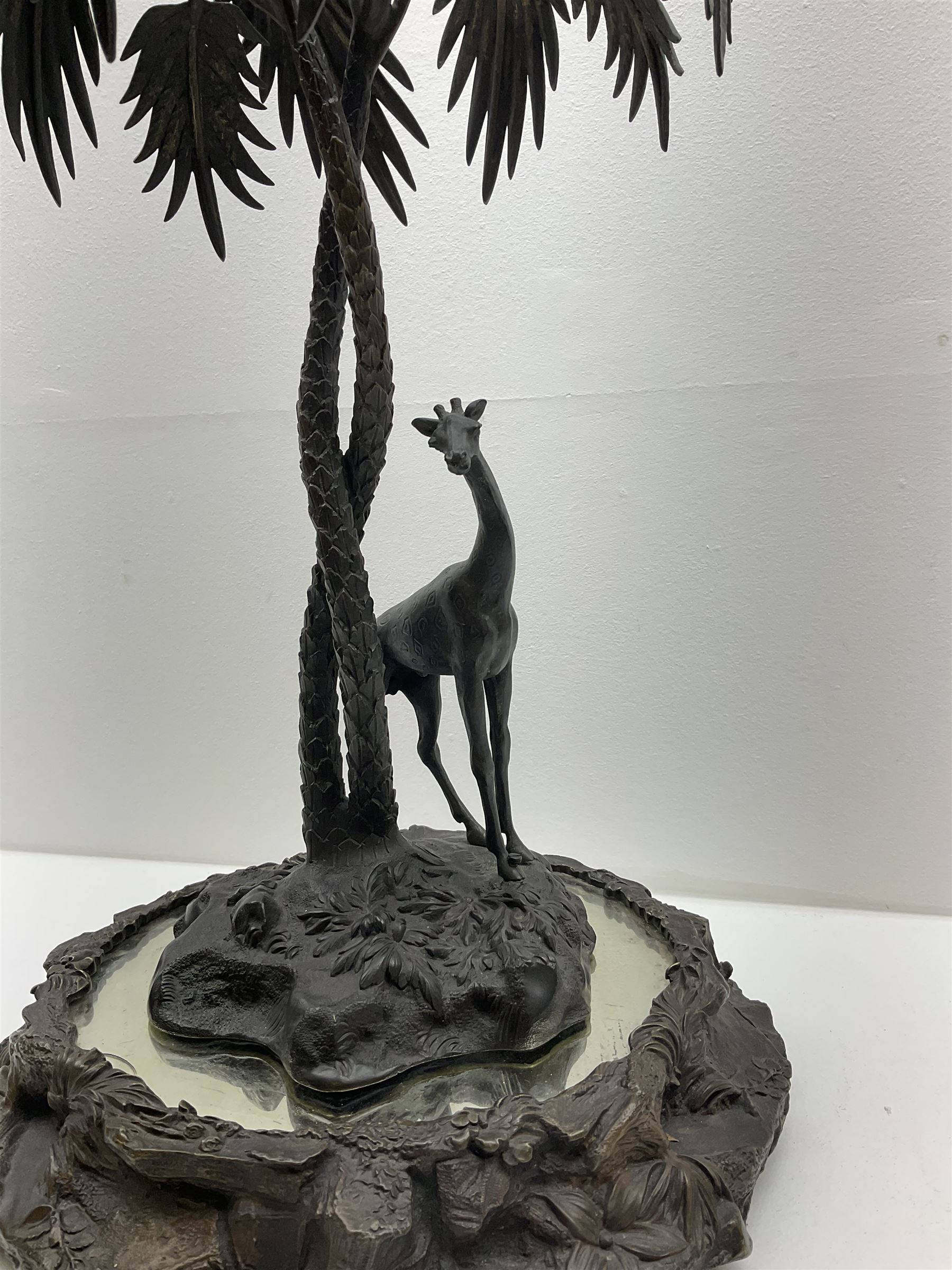 Sculpture of a giraffe under a palm tree upon a mirrored base, H48cm