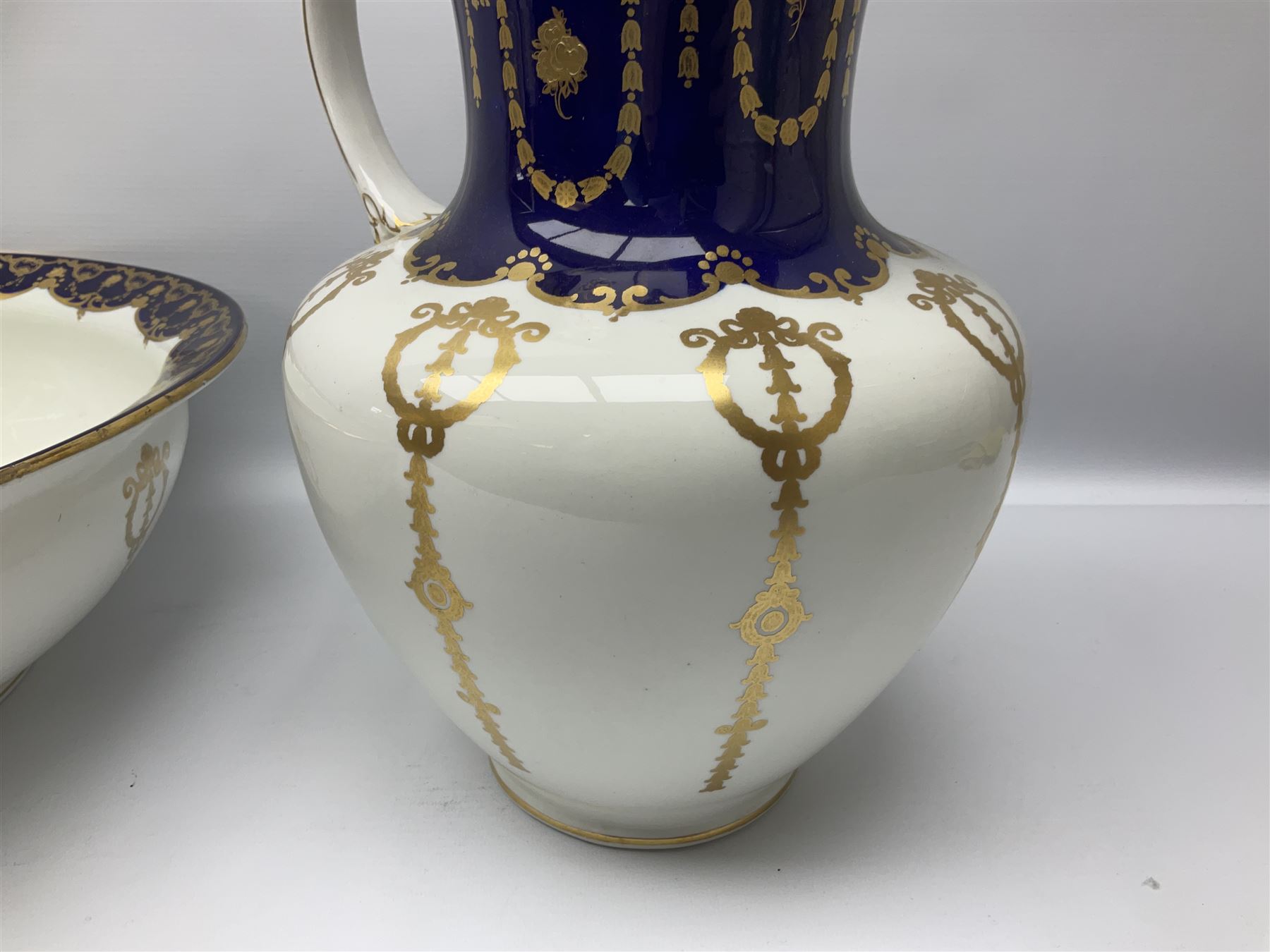 Early 20th century Bishop and Stonier four piece toilet set, comprising washbowl, wash jug, toothbrush pot, and chamber pot, each  decorated with deep blue band and husk swags and festoons in gilt, with printed Caduceus Bisto marks beneath and printed retailers mark 'Manufactured for Harrods Limited London', wash bowl D43cm, wash jug H31.5cm