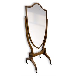 S. & H. Jewell - Edwardian mahogany cheval dressing mirror, shield shaped bevel edged mirror plate within an inlaid mahogany frame, supported by a pair of curved uprights topped with finials and terminating in a scroll design with floral inlay, the reverse bearing makers plaque, standing on four shaped supports fitted with brass castors