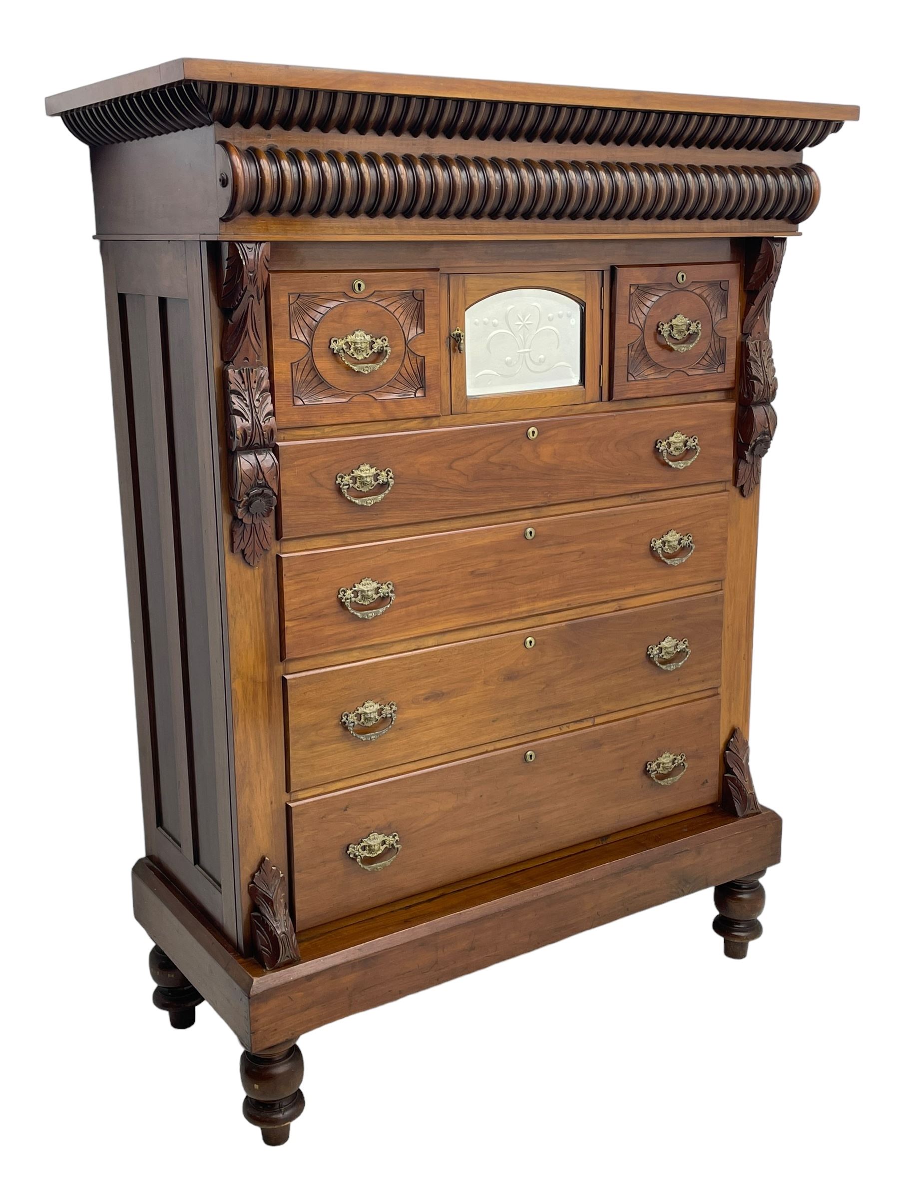 Late Victorian walnut Scotch chest, projecting cornice with turned quarter column mounts over matching half column to frieze, fitted with two upper short drawers with central cupboard, bevelled mirror glazed cupboard door, four graduating drawers below, foliage and flower head carved brackets to the uprights, panelled sides, chamfered plinth on turned feet