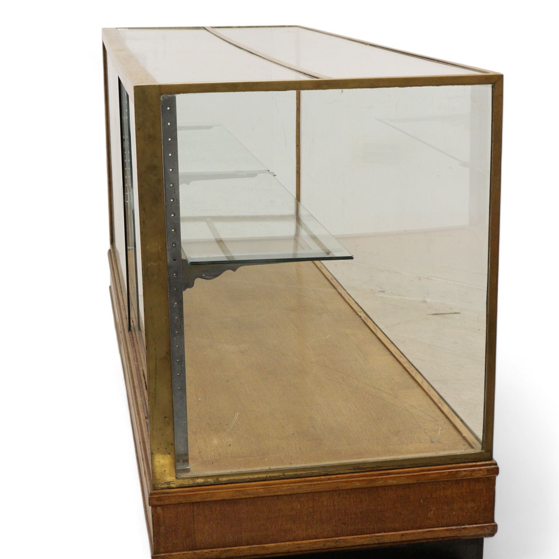 Early 20th century glazed oak and brass bound shop's display cabinet or haberdashery cabinet, fitted with two sliding glass doors, two glass shelves on chromed metal supports, black finish block feet