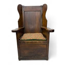 George III oak lambing chair, tall rectangular panelled backrest with shaped wings over broad scrolled armrests, box seat with removable geometric upholstered cushion, integrated drawer to lower section, resting on square supports