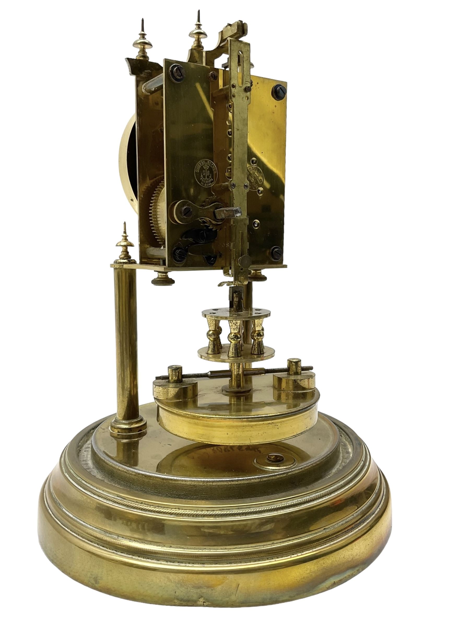 Gustav Becker - German torsion clock, serial No 2086578, on a circular brass base with a glass dome, silvered dial with Arabic numerals and steel spade hands, circular oscillating pendulum, torsion spring intact.