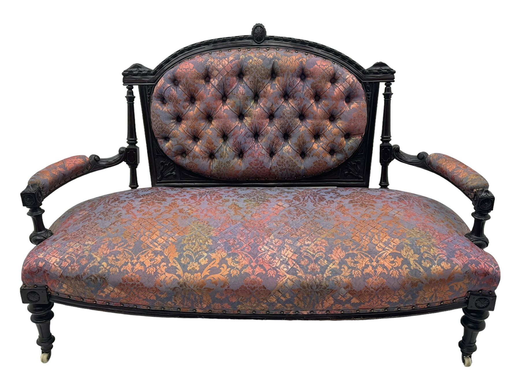 Late Victorian ebonised oak sofa, upholstered in muted purple fabric with iridescent floral pattern and nailhead trim, button-tufted backrest with carved crest rail and turned finials, scrolled padded arms supported by turned uprights, on turned supports with ceramic castors