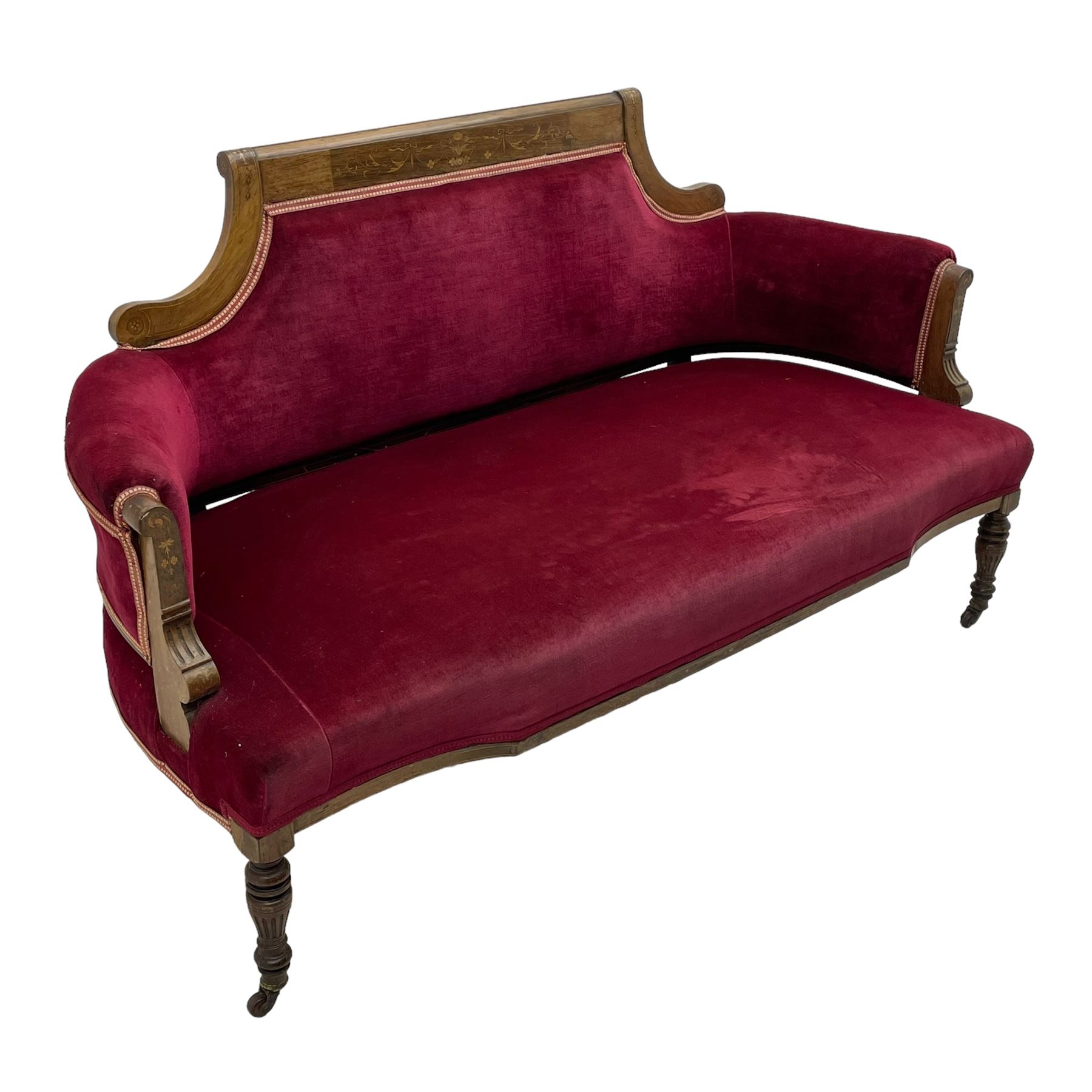 Late Victorian inlaid walnut two seat settee, the shaped cresting rail decorated with foliate inlays and boxwood stringing, upholstered in crimson velvet with sprung seat, raised on turned and fluted supports with ceramic castors