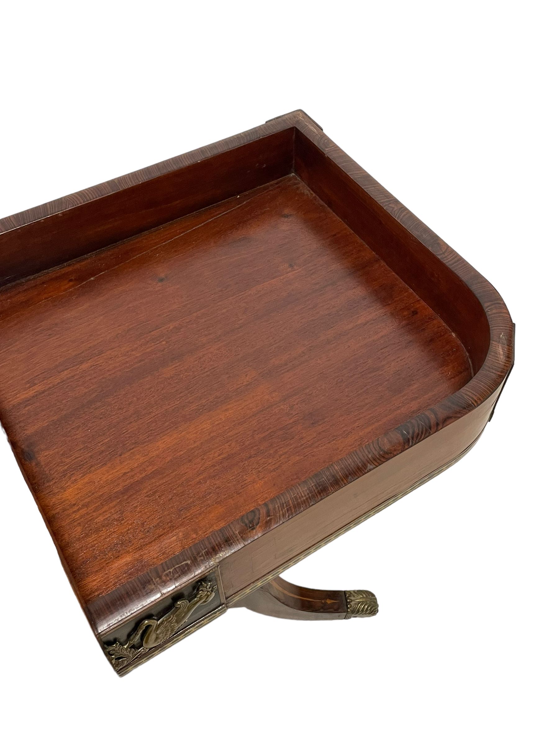 Regency inlaid rosewood card table, rectangular swivel and fold-over top with rounded corners and baize lined interior, the frieze decorated with a central ebony panel with applied gilt metal swan motifs, over a brass inlay band, raised on S-scroll supports united by concave platform base, terminating to out-splayed supports with brass cups and castors