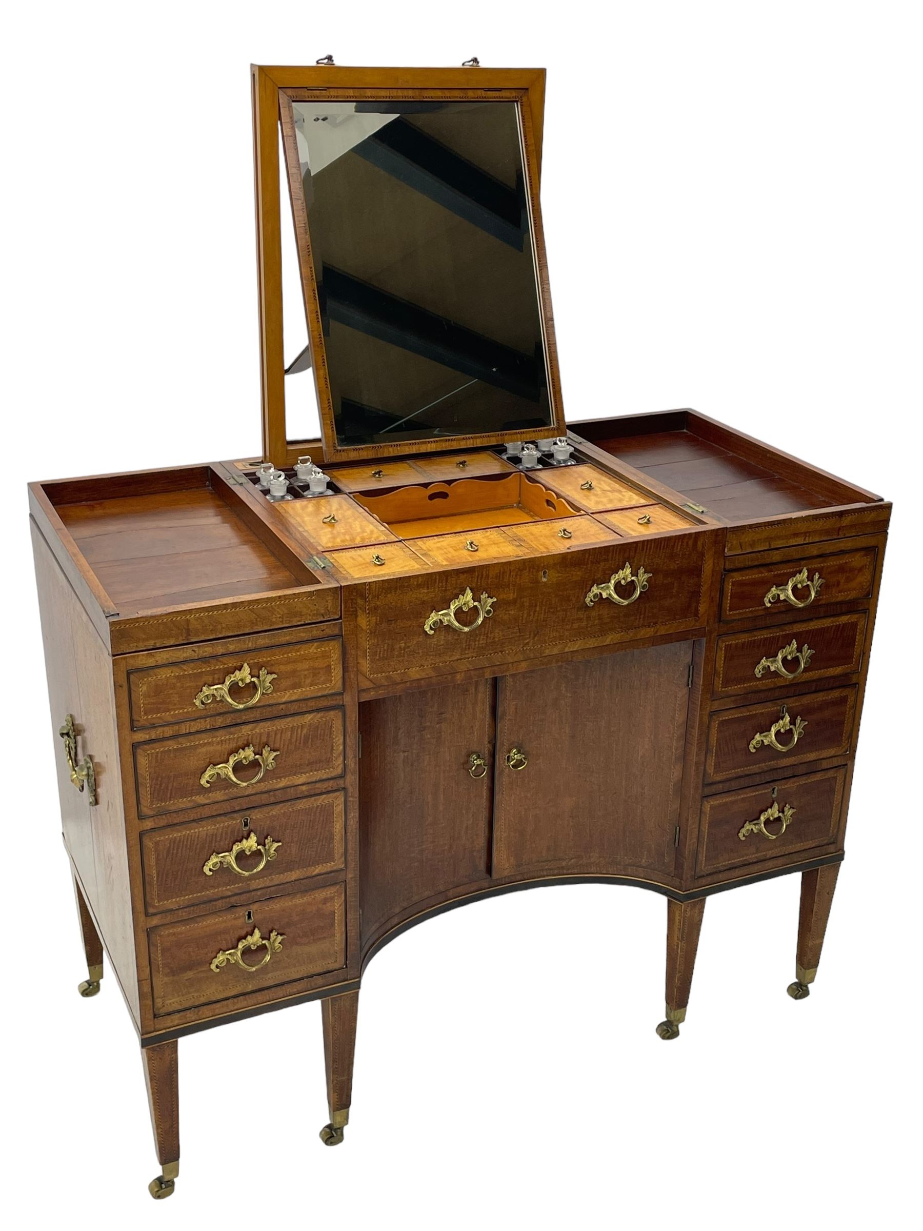 Late 19th century mahogany and satinwood dressing chest, the raised middle section hinges to reveal an interior fitted with lidded compartments, removable tray, single drawer and glass scent bottles, lift-up bevelled mirror with adjustable hinged mechanism, fitted with a further eight cock-beaded graduating drawers and curved kneehole with double cupboard, square tapering supports on brass cups and castors, inlaid throughout with checkered stringing, ornate Rococo cast gilt metal handles