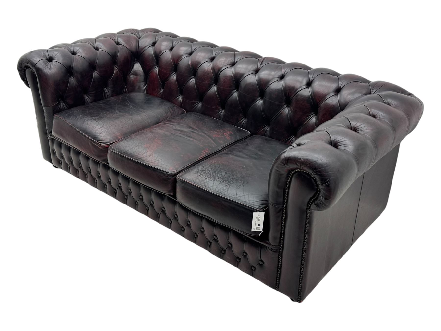 Chesterfield three-seat sofa, traditional shaped upholstered in deeply buttoned dark red leather; together with similar footstool 