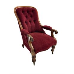 Victorian mahogany framed open armchair, upholstered in buttoned red fabric, the arm terminals carved with scrolls, on turned front supports with brass cups and castors